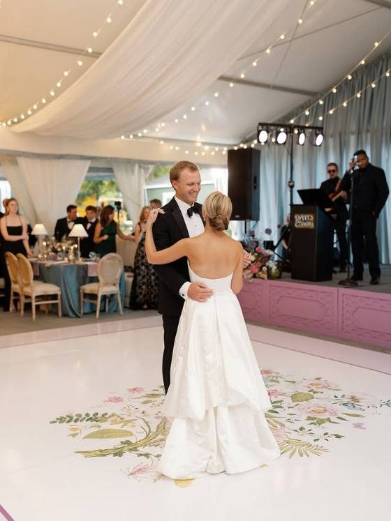 Couple dancing on a floral-bordered dance floor wrap at a tented reception