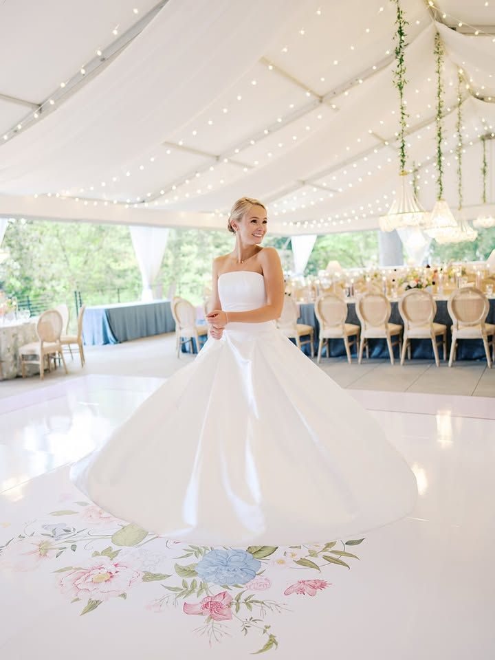 Bride standing on a custom floral dance floor wrap under a tented wedding reception