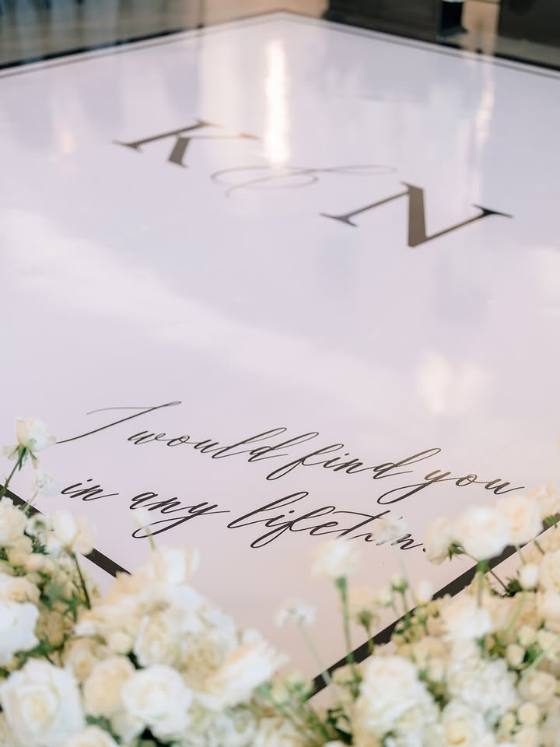 Close-up of a custom dance floor wrap with couple initials and script lettering surrounded by white florals